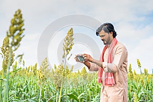 Happy young farmer checking crop growth by taking photos on mobile phone app at farmland - concept of technology, modern