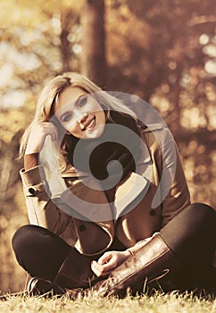 Happy young fashion blond woman sitting on the grass in autumn forest