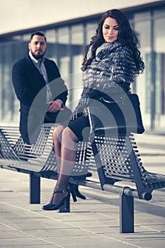 Happy young fashion couple sitting on bench on city street