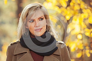 Happy young fashion woman in beige coat walking in autumn park