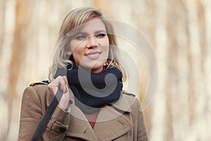 Happy young fashion woman in beige coat walking in autumn park