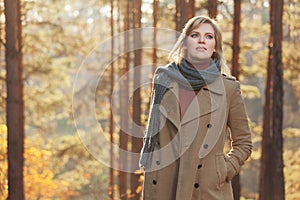 Happy young fashion woman in beige coat walking in autumn park