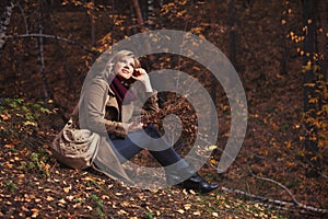 Happy young fashion woman with handbag sitting on ground in autumn park