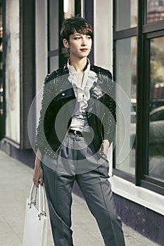 Happy young fashion woman in leather jacket with handbag in a city street