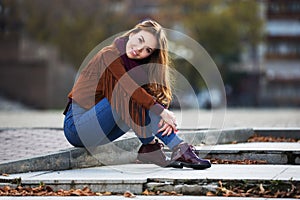 Happy young fashion woman in leather jacket sitting on sidewalk