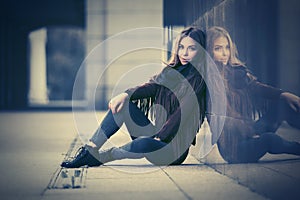 Happy young fashion woman in leather jacket sitting at the wall