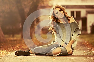 Happy young fashion woman in ripped jeans sitting on sidewalk