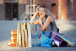 Happy young fashion woman with shopping bags sitting on sidewalk