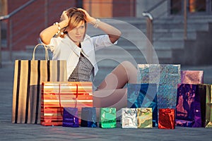 Happy young fashion woman with shopping bags sitting on sidewalk