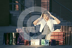 Happy young fashion woman with shopping bags sitting on sidewalk