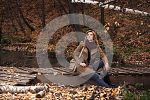 Happy young fashion woman sitting on wooden bridge in autumn park