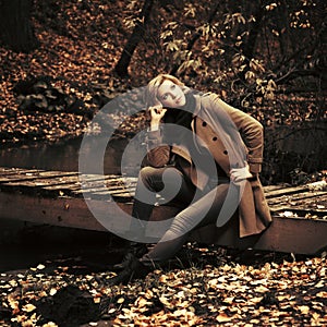Happy young fashion woman sitting on wooden bridge in autumn park