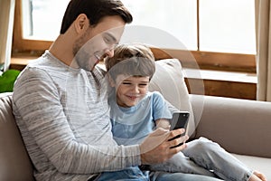 Happy young father cuddling little son, showing funny mobile applications.