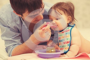 Happy young father feeding baby girl on blanket