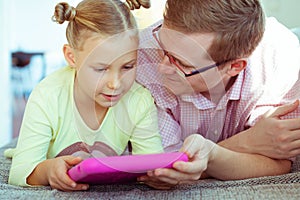 Happy young father have fun with his little daughter working with tablet at home on couch