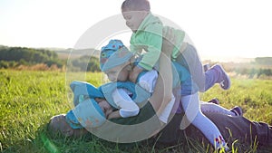 Happy young father with his children lies on the lawn in the park. Three happy children play with their father. Children