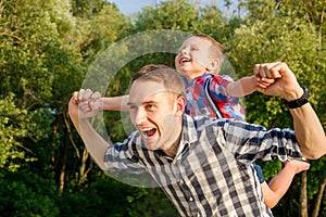 Happy young father holds his son piggyback ride on his shoulders