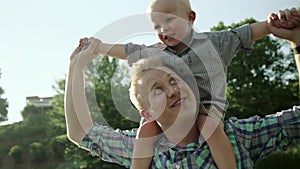 Happy young father holds his son piggyback ride on his shoulders and looking up. Little boy is sitting piggyback on