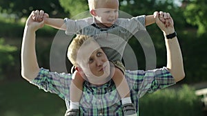 Happy young father holds his son piggyback ride on his shoulders and looking up. Little boy is sitting piggyback on