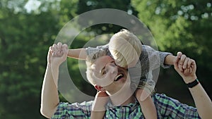 Happy young father holds his son piggyback ride on his shoulders and looking up. Little boy is sitting piggyback on