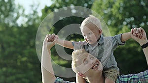 Happy young father holds his son piggyback ride on his shoulders and looking up. Little boy is sitting piggyback on