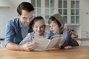 Happy young father reading paper book to little kids.