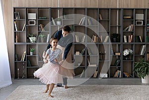 Happy young father and small daughter dancing at home.