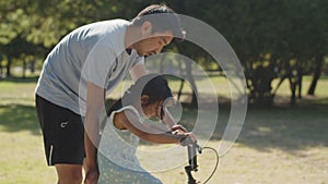 Happy young father teaching his daughter to ride bike in park