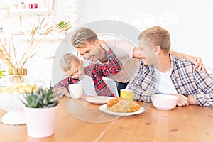 Happy young fathers and son have breakfast in the kitchen, gay family with a child, time together, parenting in homosexual