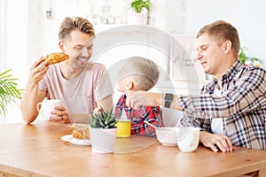 Happy young fathers and son have breakfast in the kitchen, gay family with a child, time together, parenting in homosexual