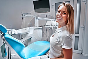 Happy young female dentist with tools over medical office background