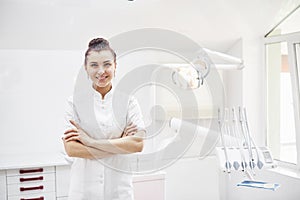 Happy young female dentist with tools over medical office background. Stomatology and healthcare concept