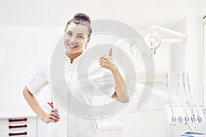 Happy young female dentist with tools over medical office background. Stomatology and healthcare concept