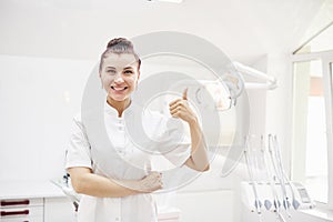 Happy young female dentist with tools over medical office background. Stomatology and healthcare concept