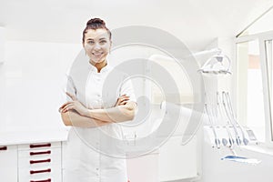 Happy young female dentist with tools over medical office background. Stomatology and healthcare concept