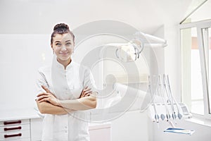 Happy young female dentist with tools over medical office background. Stomatology and healthcare concept