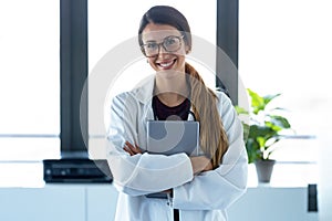 Happy young female doctor smiling and looking at camera while digital tablet and standing in the consultation