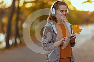 happy young female in fitness clothes in the park with autumn leaf and headphones