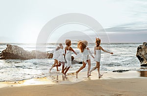 Happy young female friends having fun and celebrating hen party while running on the beach at the sunset