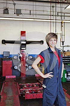 Happy young female mechanic with hands on hips in automobile repair shop