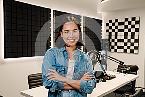 Happy young female radio host smiling while broadcasting in studio