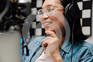 Happy young female radio host using microphone and headphones while broadcasting in studio