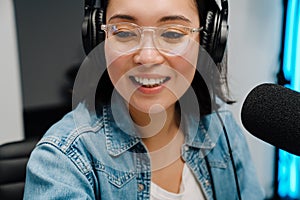 Happy young female radio host using microphone and headphones while broadcasting in studio