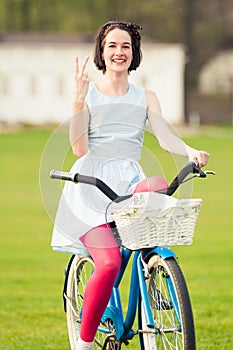 Happy young female standing on bicycle and showing victory gestu