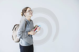 Happy young female student looking upwards carrying back pack holding books