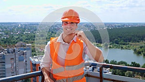 Happy young foreman in construction uniform and safety hardhat standing on the roof while posing at camera. Business