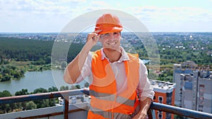 Happy young foreman in construction uniform and safety hardhat standing on the roof while posing at camera. Business