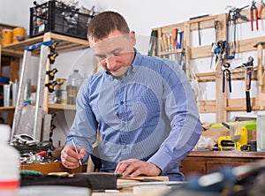 young male carpenter working wood plank at workshop