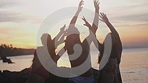 Happy young friends with children having fun singing song and dancing rising their hands on a tropical beach during