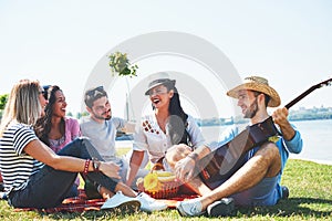 Happy young friends having picnic in the park.They are all happy,having fun,smiling and playing guitar